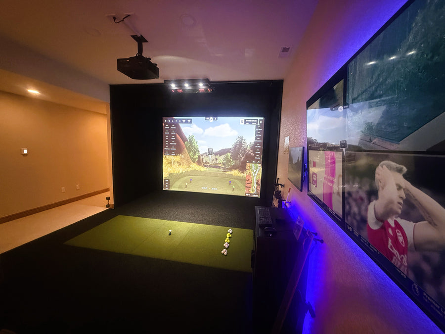 Indoor golf simulator setup with screen displaying a golf course and wall-mounted TV showing a sports event.