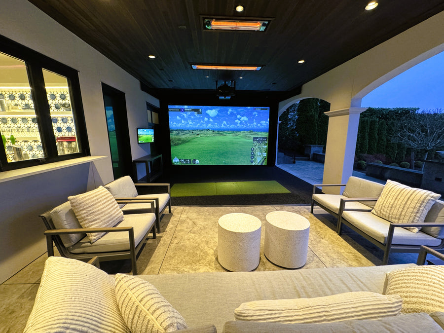 Indoor living room with a large screen and an outdoor golf simulator, surrounded by comfortable seating and decor.