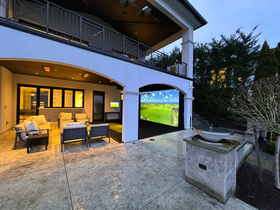 Outdoor living space with a golf simulator, surrounded by trees and a house.