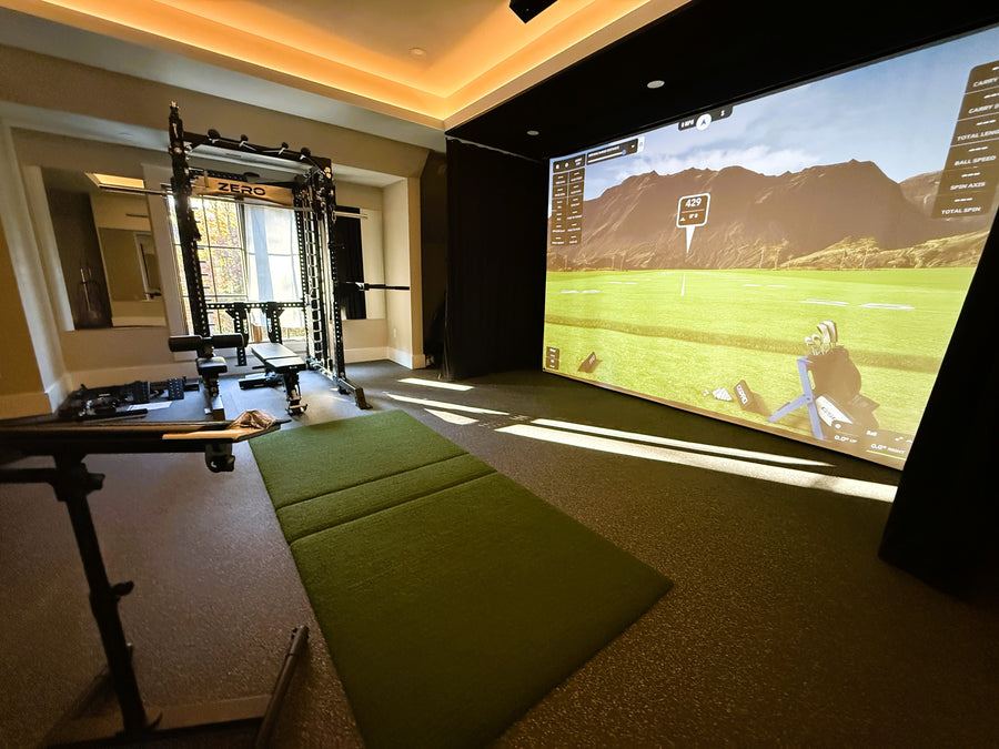 Golf simulator setup in a home gym with a large screen displaying a golf course.