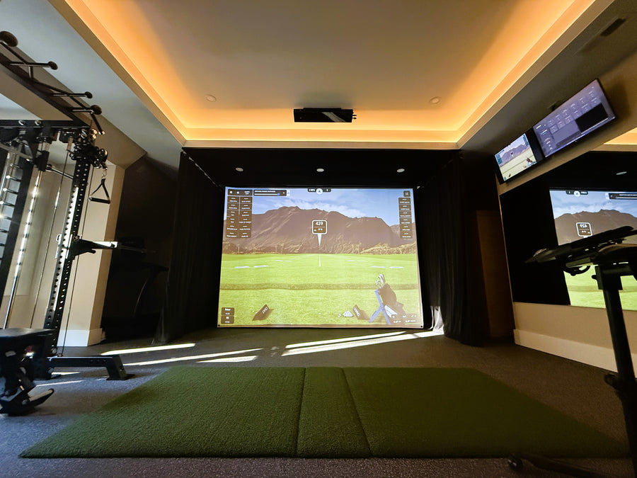 Indoor golf simulator setup with screens and a green mat on the floor.
