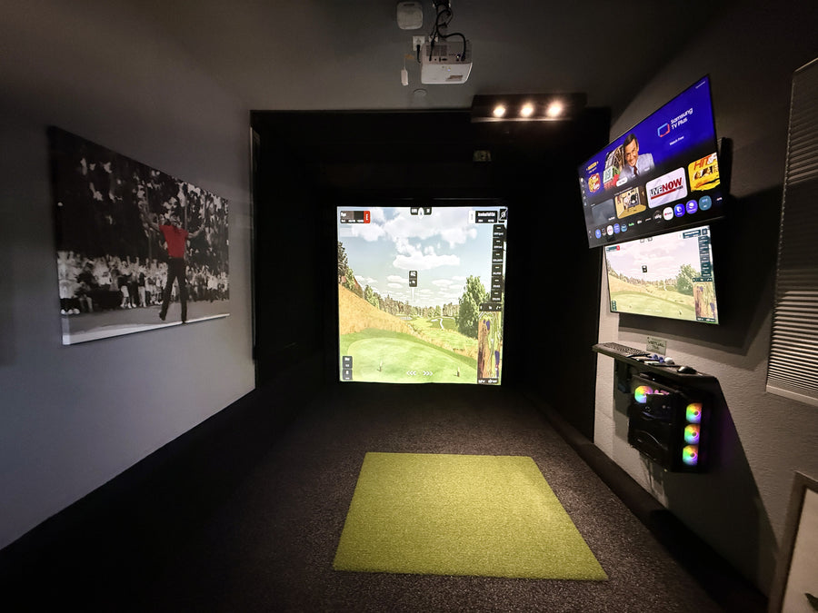 Golf simulator setup with multiple screens and a green mat on the floor.