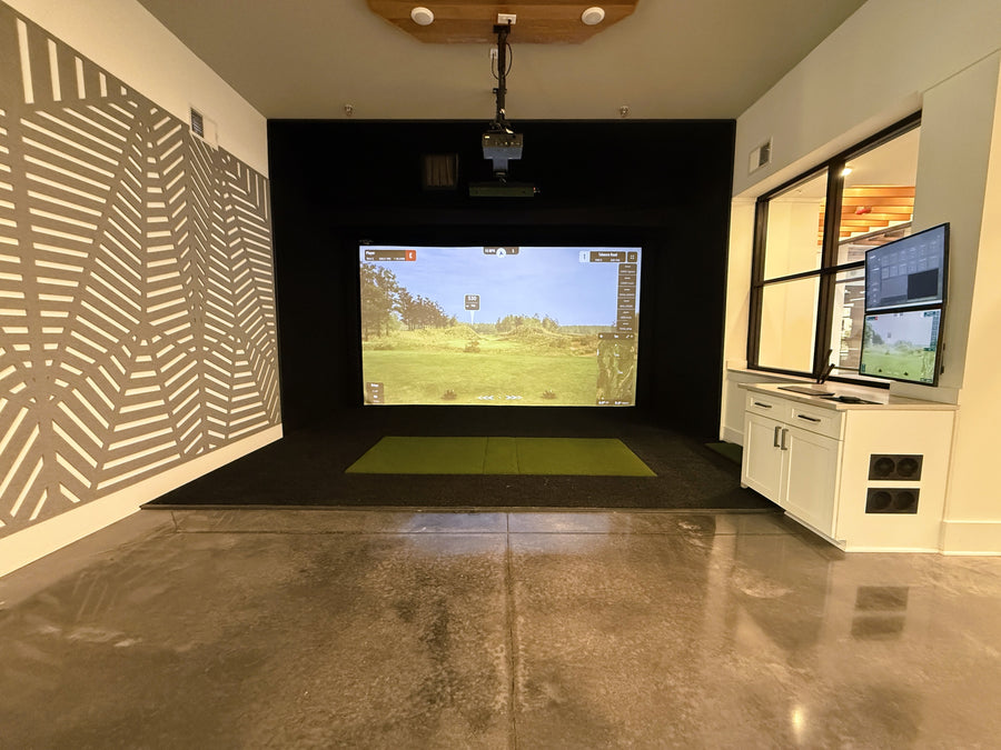 Indoor golf simulator setup in a modern room with a screen displaying a golf course.