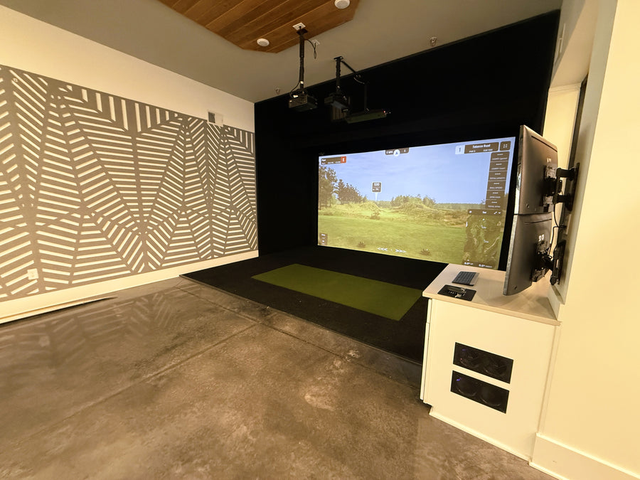 Golf simulator setup in a room with a large screen displaying a golf course.