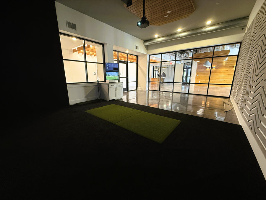 Modern interior with a golf simulator, large windows, and a desk.