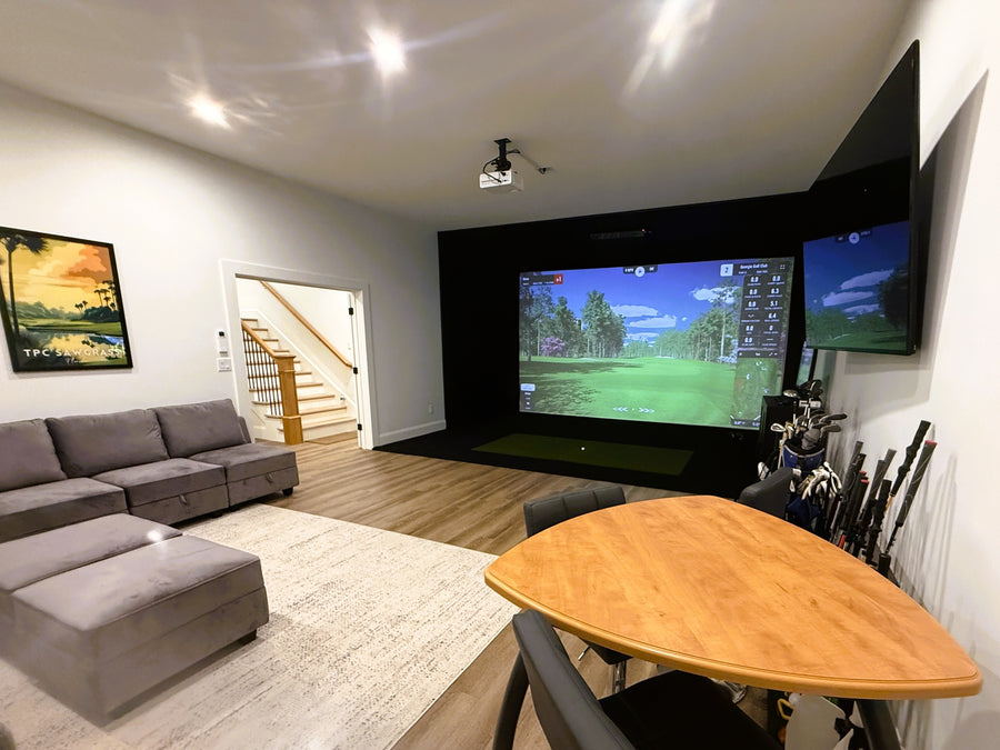 Golf simulator room with a large screen displaying a golf simulation game, surrounded by furniture.