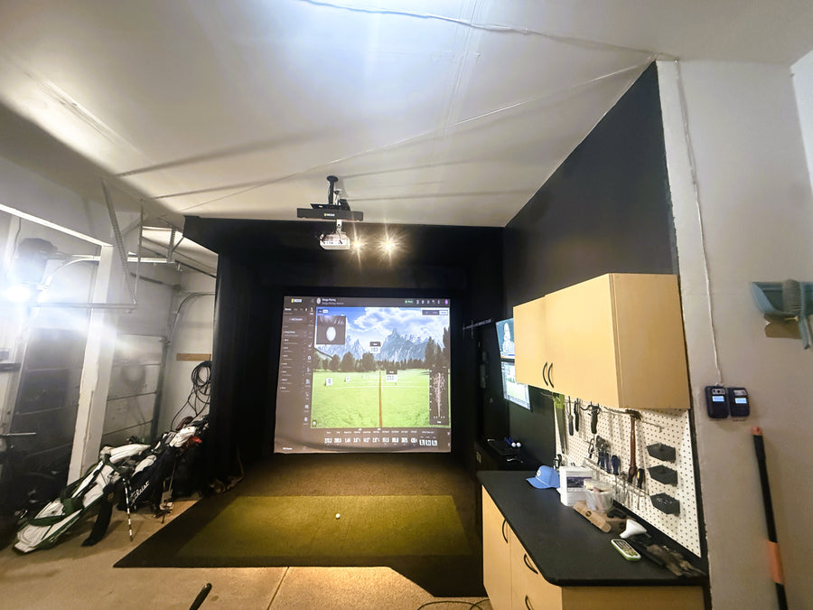 Indoor golf simulator setup with projection screen and golf equipment.