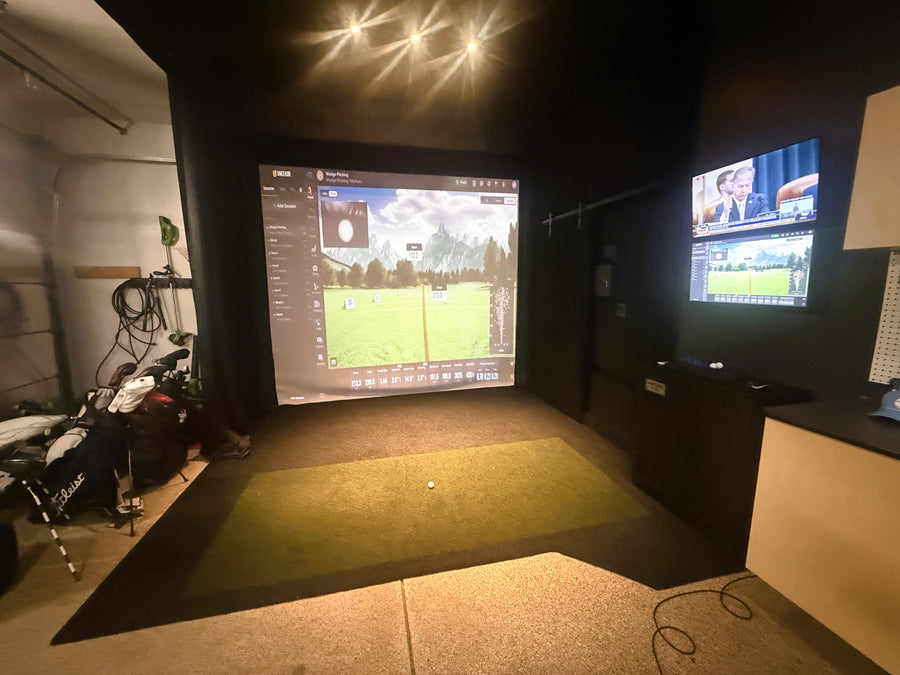 Indoor golf simulator setup with two screens displaying golf simulation software.
