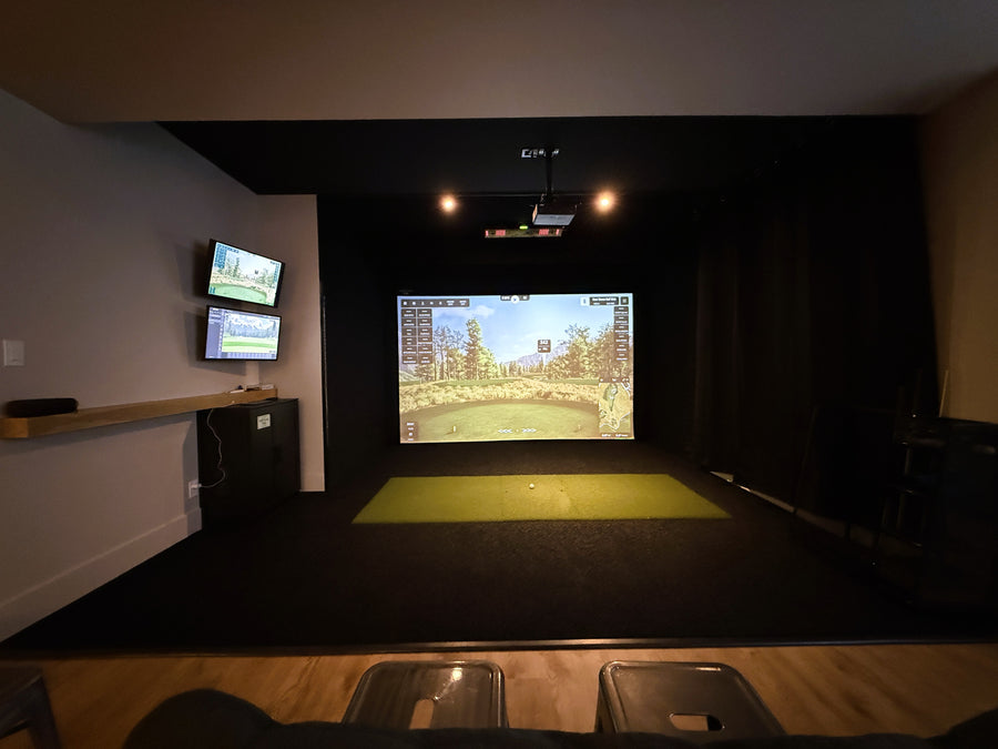 Indoor golf simulator setup with multiple screens and a projection on the wall.