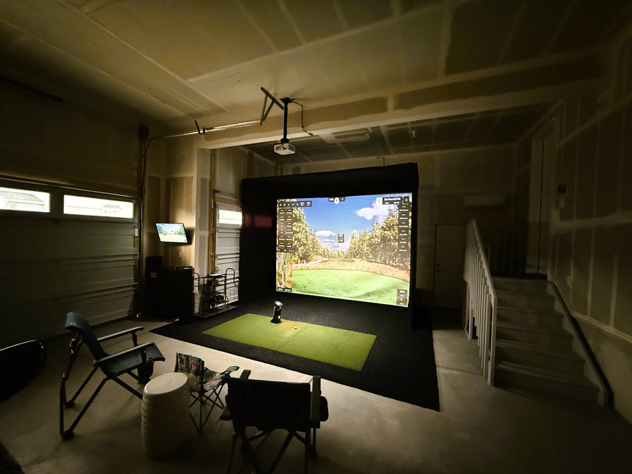 Indoor golf simulator setup in a room with a screen displaying a golf course.