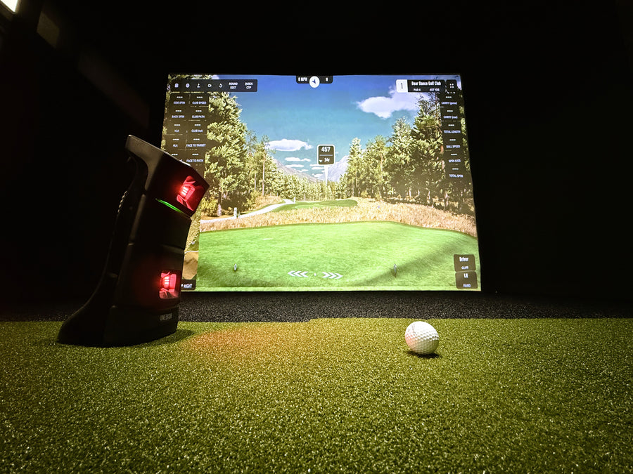 Golf simulator setup with screen displaying a golf course, golf club, and ball on grass.