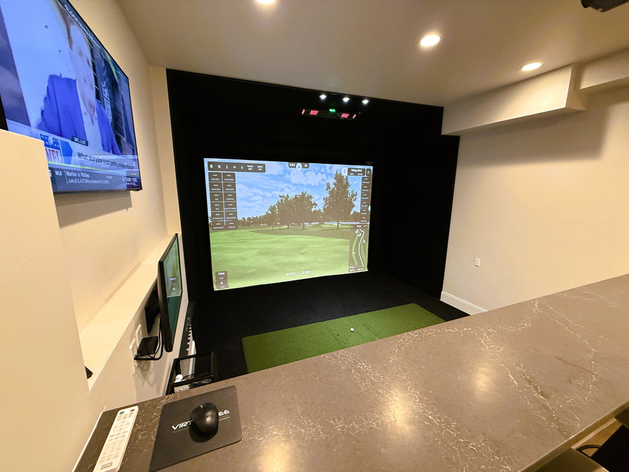 Golf simulator setup in a room with multiple screens and a counter.