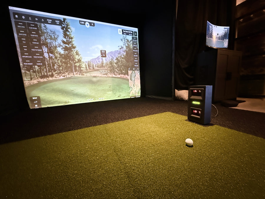 Golf simulator setup with screen displaying a golf course and ball on the floor.