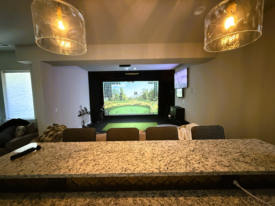 Living room with a large screen and golf simulator, surrounded by chairs and a coffee table.