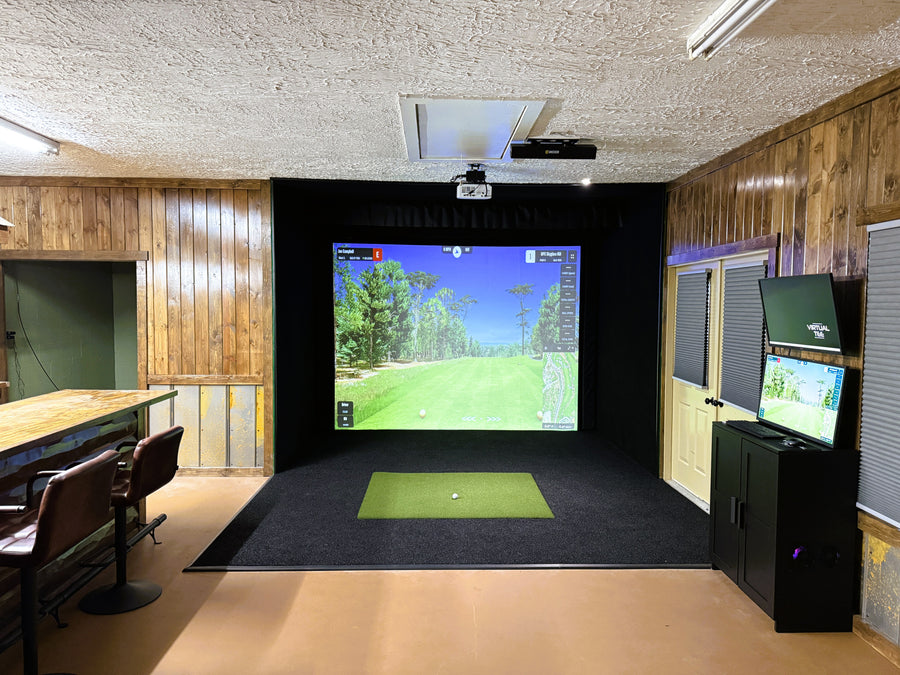 Indoor golf simulator setup in a room with wooden walls and a screen displaying a golf course.