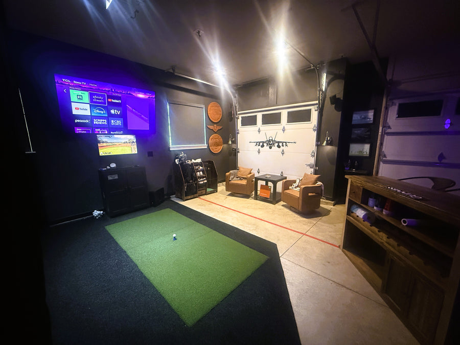Garage with seating and fighter jet artwork on the garage door. Golf simulator in the corner with green turf on the ground. 