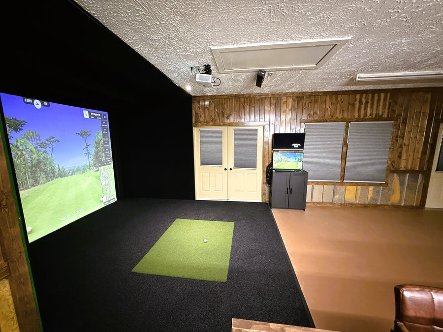 Golf simulator room with screen displaying a golf course and cabinets in the background.