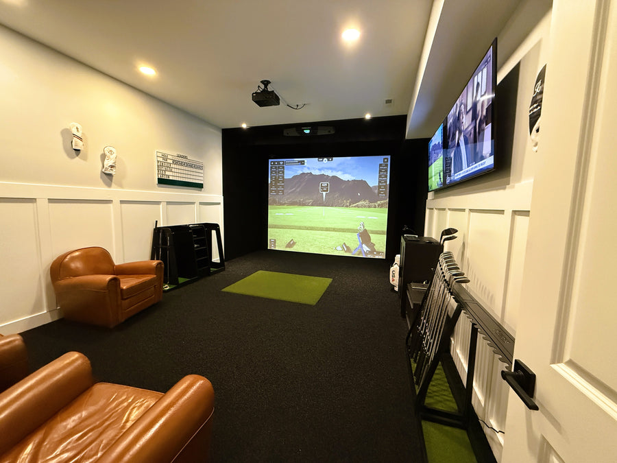 Indoor golf simulator setup with a large screen displaying a video game, surrounded by brown leather chairs.