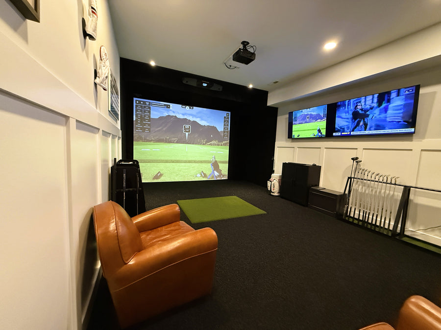 Indoor golf simulator setup with two TVs displaying video games, a brown leather chair, and a green rug.