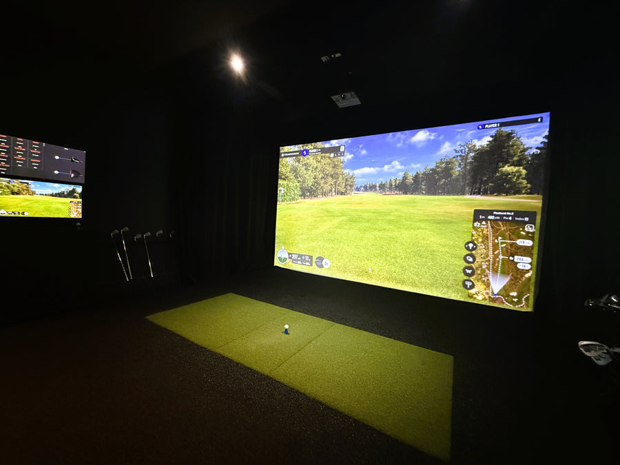 Indoor golf simulator setup with large screen displaying a golf course.