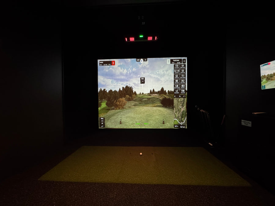 Golf simulator setup with screen displaying a golf course in a dark room