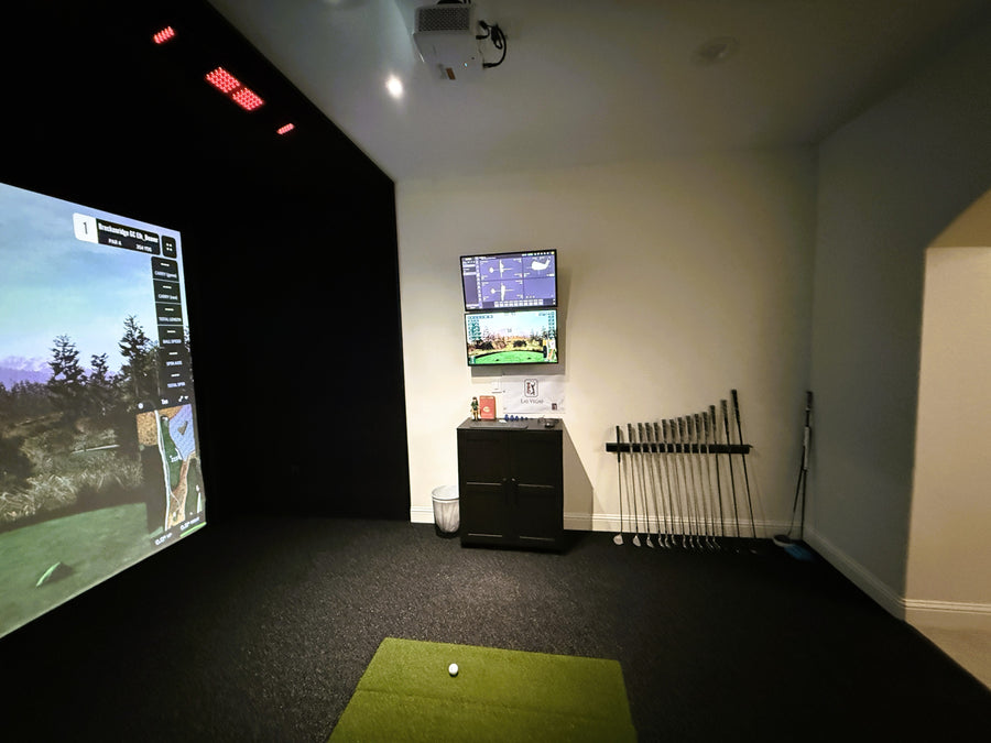 Golf simulator setup with screens, golf clubs, and a ball on a green mat.