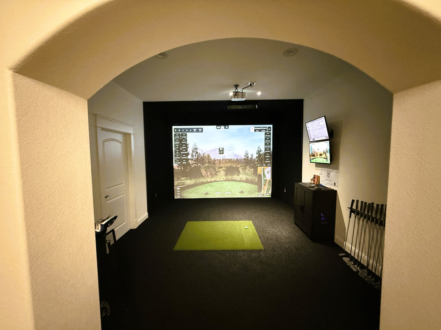 Golf simulator setup in a room with a screen displaying a golf course.