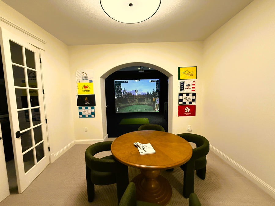 Game room with a round wooden table and chairs, with a golf simulator in the next room.