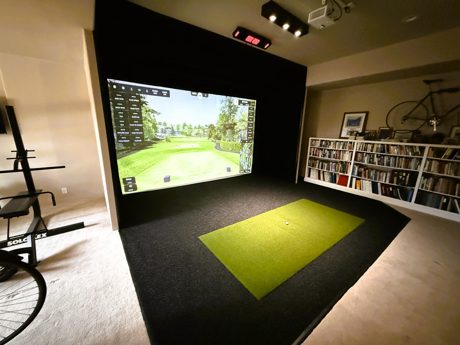 Golf simulator setup in a room with a large screen displaying a golf course.