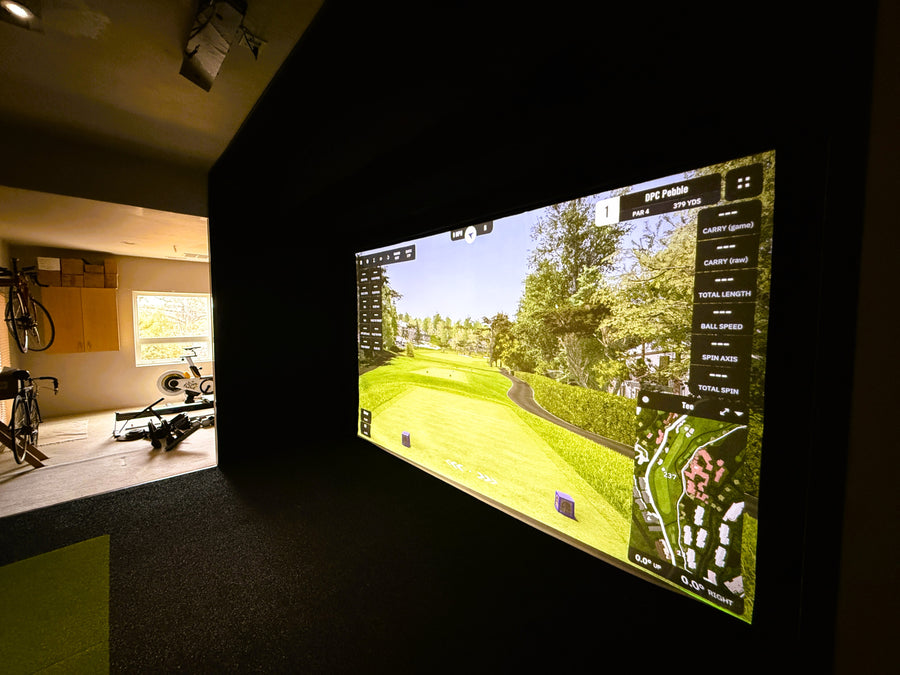 Golf simulator setup in a room with a large screen displaying a golf course.