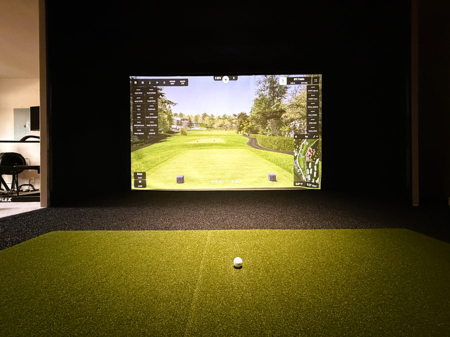 Golf simulator setup with screen displaying a golf course and ball on a green floor.