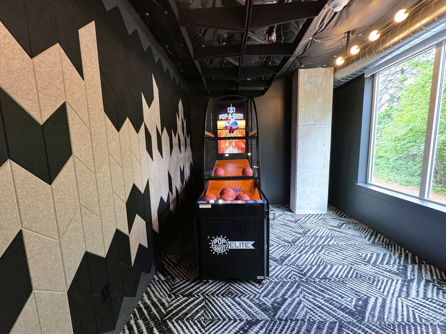 Indoor game room with arcade machine against a geometric-patterned wall.