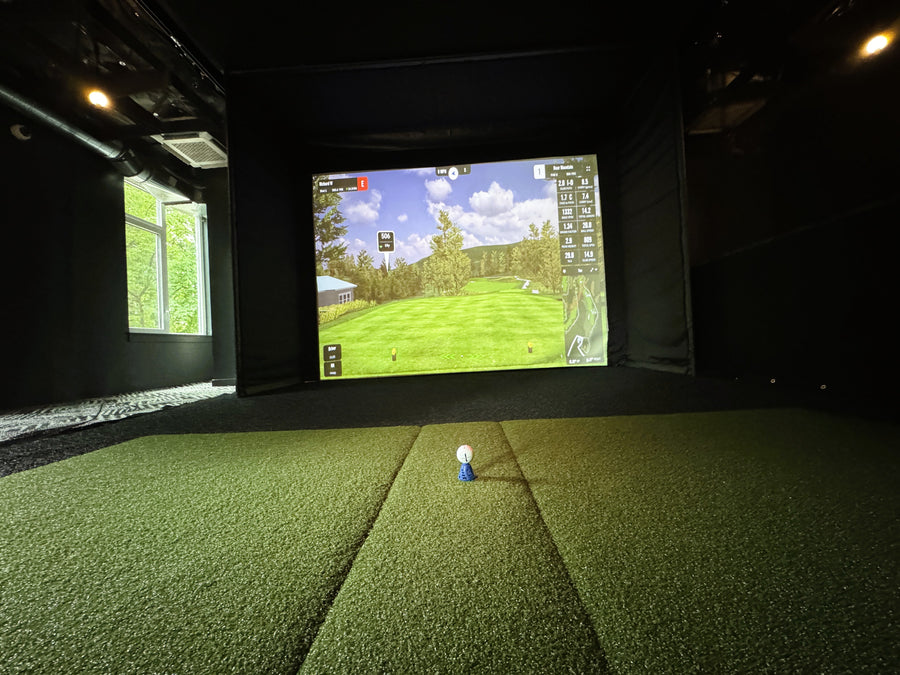 Indoor golf simulator with green turf and screen displaying a golf course.
