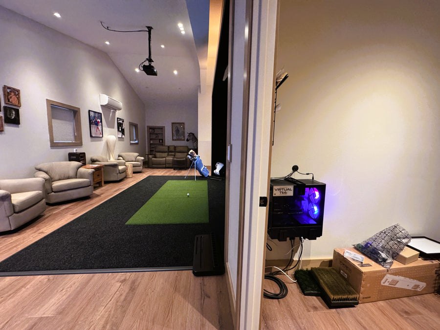 Indoor golf simulator green setup in a living room with a projector screen and equipment.