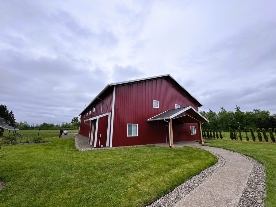 Red barn with a gravel path leading up to it under a cloudy sky.