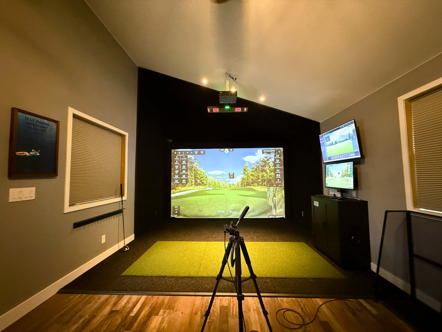 Indoor golf simulator setup with projection screen and golf simulator device.