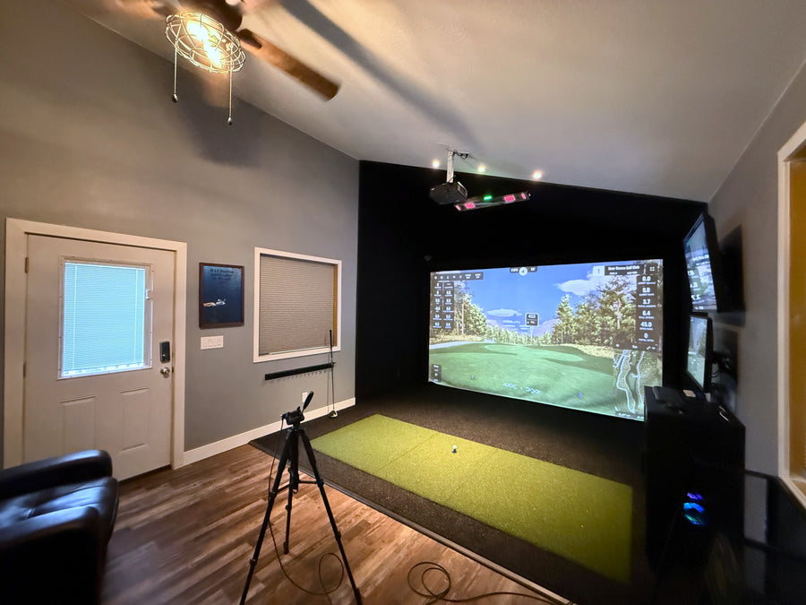 Indoor golf simulator setup in a room with a screen displaying a golf course.