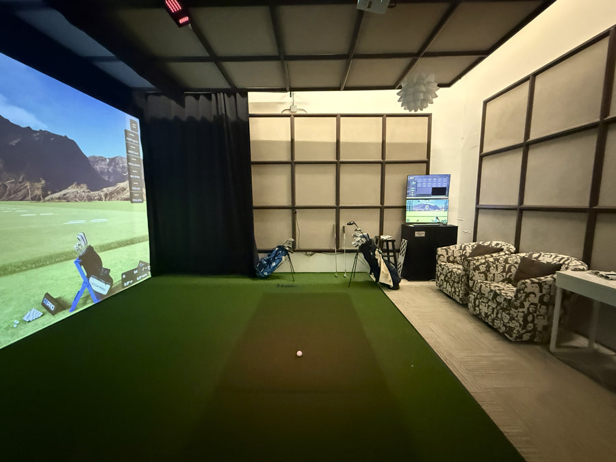 Indoor golf simulator setup in a room with a screen displaying a golf course.
