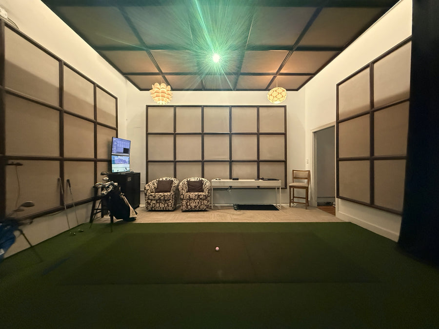 Indoor putting green with golf simulator setup in a room with walls and ceiling panels.
