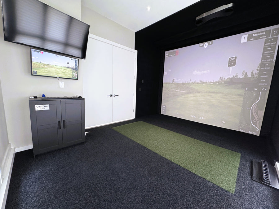 Golf simulator setup in a room with two screens displaying a golf course.