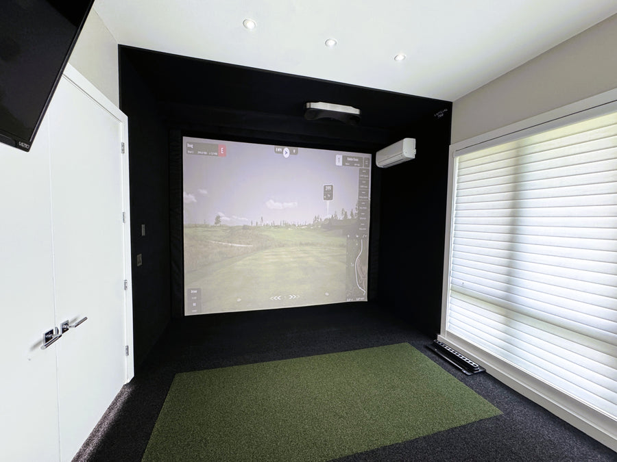 Indoor golf simulator setup with screen and green turf floor.