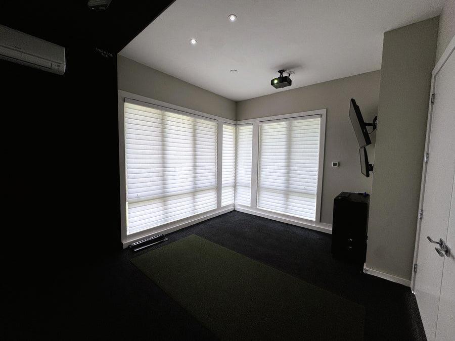 Corner of golf simulator room with Tv's mounted to the wall and projector to the ceiling. 