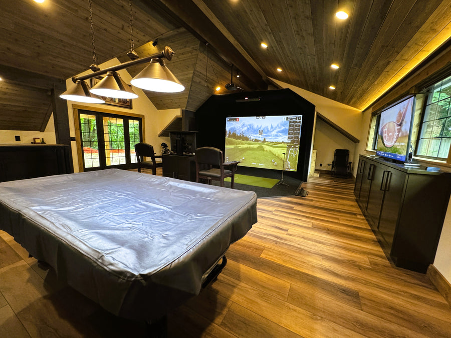 Golf simulator room with a large screen displaying a golf game, surrounded by wooden furniture and decor.