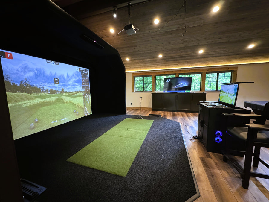 Golf simulator room with a large screen displaying a golf simulation game, surrounded by golf equipment.