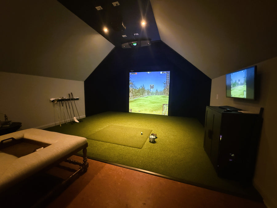 Indoor golf simulator setup with green turf and screens displaying a golf course.