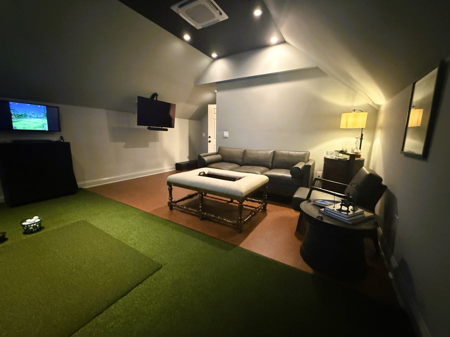 Golf simulator room with a green carpet, gray sofa, and wall-mounted TV.