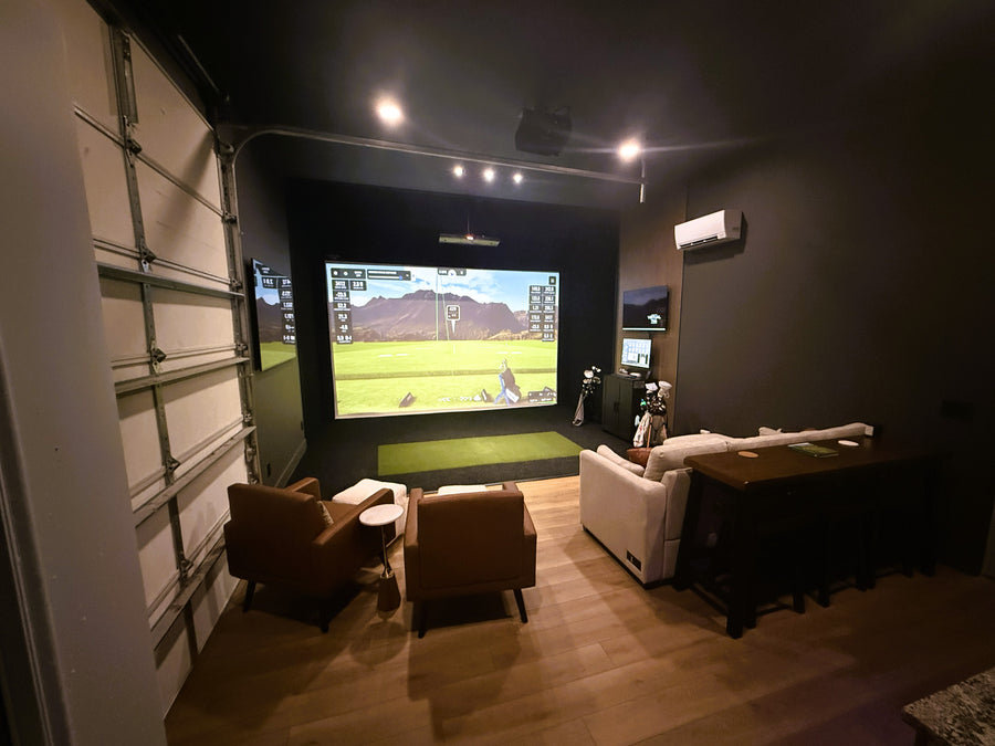Indoor golf simulator setup with a large screen displaying a game, surrounded by comfortable seating and dim lighting.