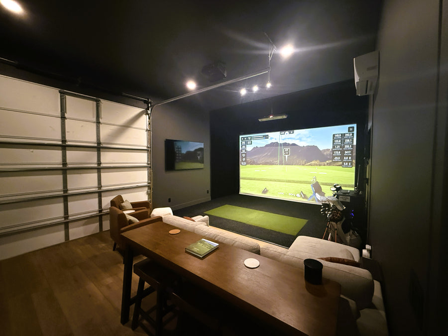 Indoor golf simulator setup with a large screen displaying a golf simulation game in an outbuilding.
