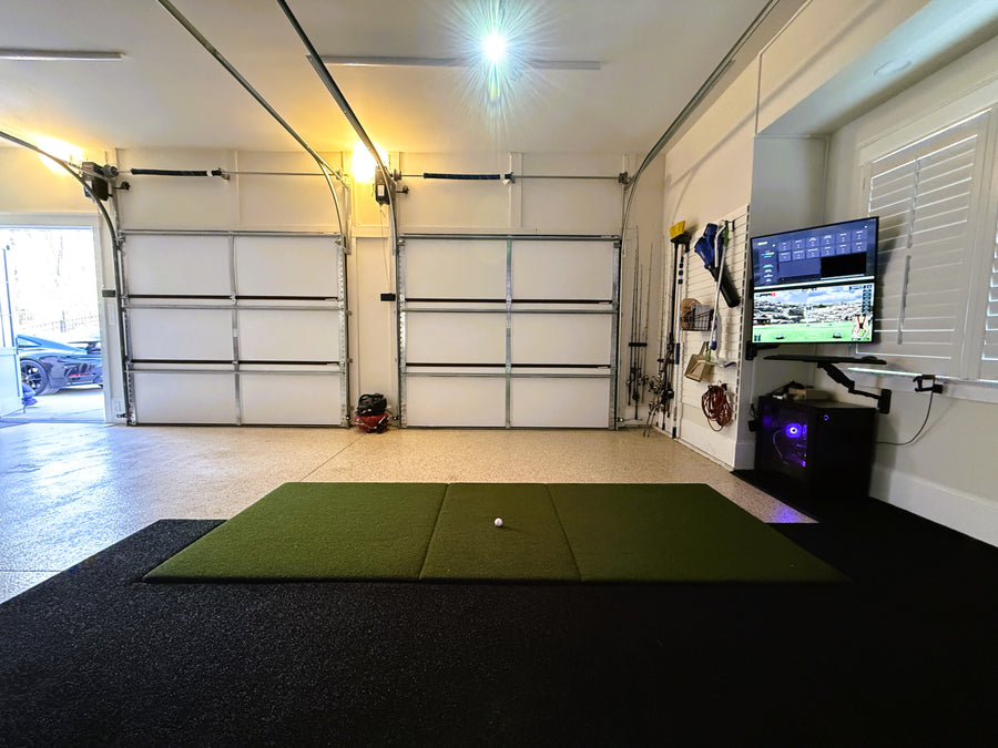 Garage with a golf simulator and a green mat, a TV displaying a sports game, and various items on the wall.