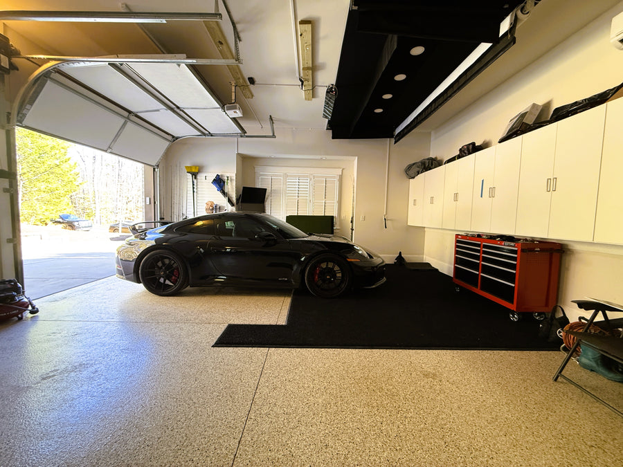 Garage with a retractable indoor golf simulator and a black sports car, tool cabinets, and a workbench.